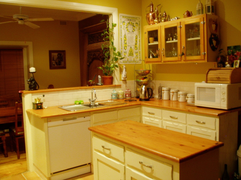 Photo of a small country u-shaped eat-in kitchen in Adelaide with a double-bowl sink, recessed-panel cabinets, white cabinets, wood benchtops, white splashback, subway tile splashback, white appliances, terra-cotta floors and with island.