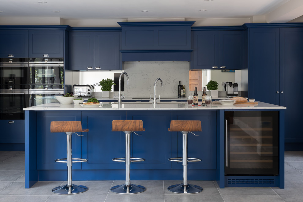 Inspiration for a large transitional u-shaped eat-in kitchen in Hertfordshire with an undermount sink, shaker cabinets, blue cabinets, quartzite benchtops, white splashback, mirror splashback, stainless steel appliances, porcelain floors, with island, grey floor and white benchtop.