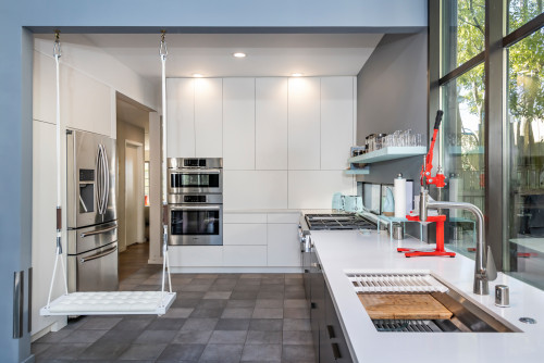 White handleless RTA cabinets with tall pantry wall, built-in ovens, long countertop run, open shelf, and large window