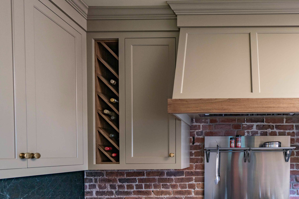 This is an example of a mid-sized country l-shaped kitchen pantry in Boston with shaker cabinets, brown cabinets, stainless steel appliances, with island, black benchtop, an undermount sink, red splashback, brick splashback, slate floors and multi-coloured floor.