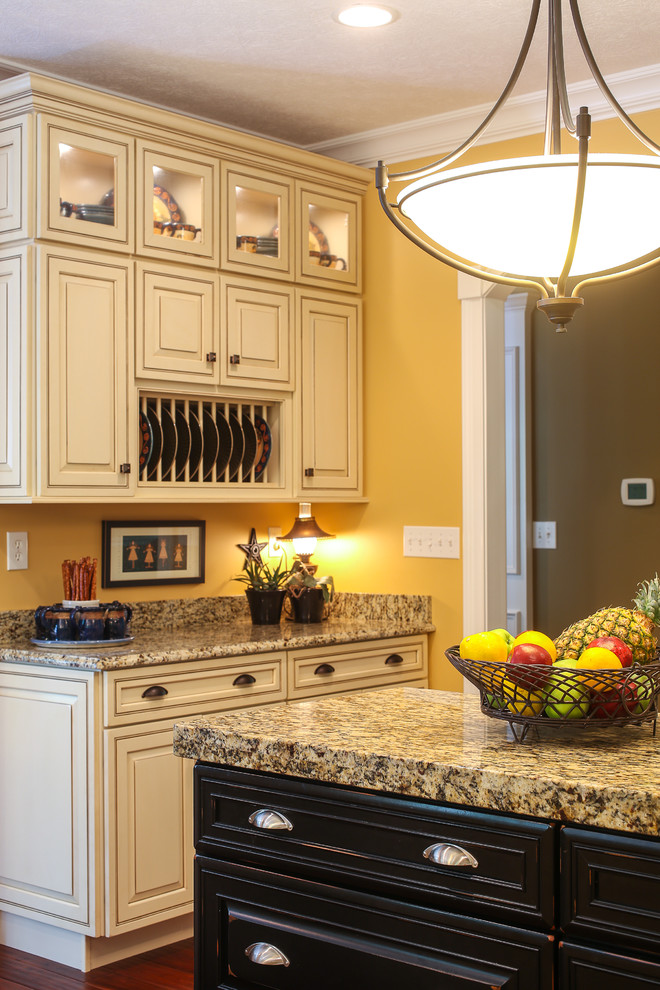 Large transitional l-shaped dark wood floor enclosed kitchen photo with a double-bowl sink, raised-panel cabinets, beige cabinets, granite countertops, yellow backsplash, stainless steel appliances and an island