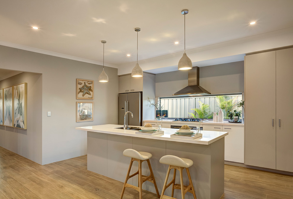Photo of a mid-sized beach style galley eat-in kitchen in Perth with an undermount sink, flat-panel cabinets, quartz benchtops, stainless steel appliances, light hardwood floors, with island and grey cabinets.