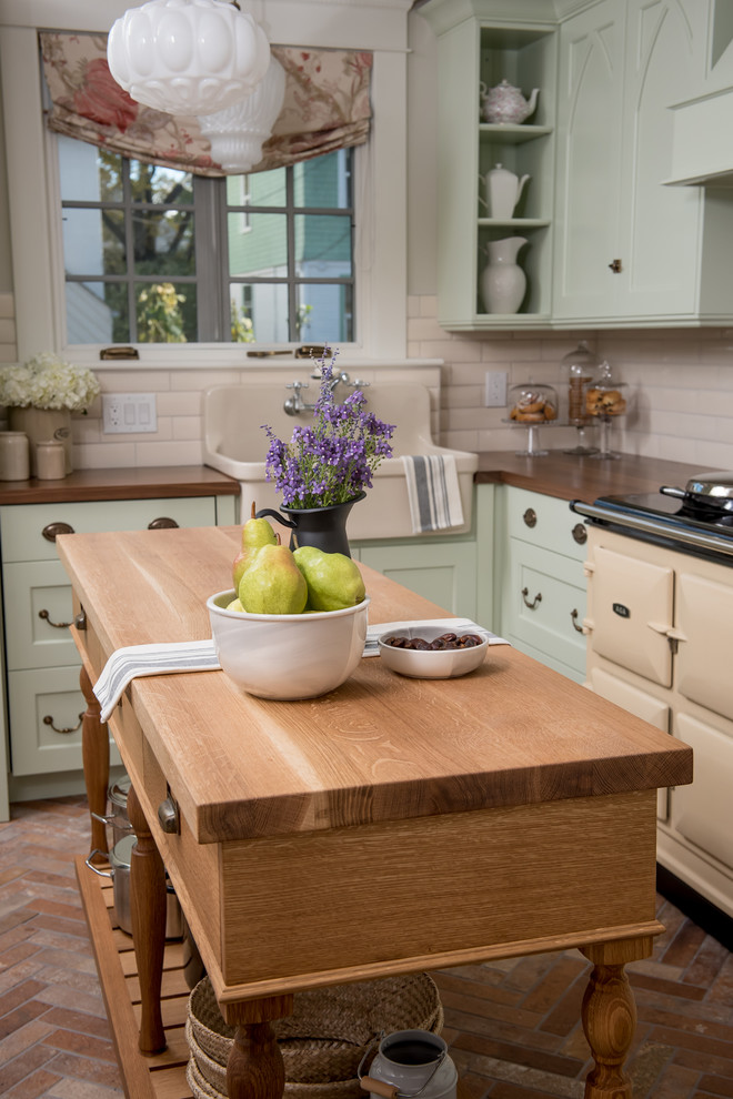 Farmhouse l-shaped porcelain tile enclosed kitchen photo with a farmhouse sink, recessed-panel cabinets, green cabinets, wood countertops, white backsplash, porcelain backsplash, colored appliances and an island