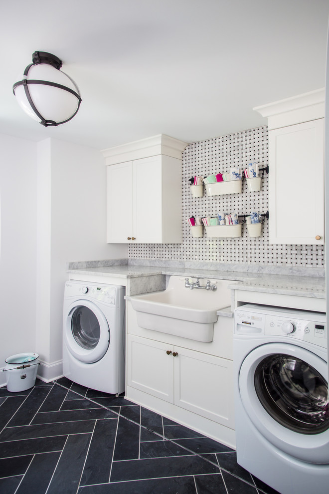 Photo of a mid-sized transitional single-wall dedicated laundry room in Toronto with a farmhouse sink, shaker cabinets, white cabinets, quartz benchtops, white walls, porcelain floors, a side-by-side washer and dryer and black floor.