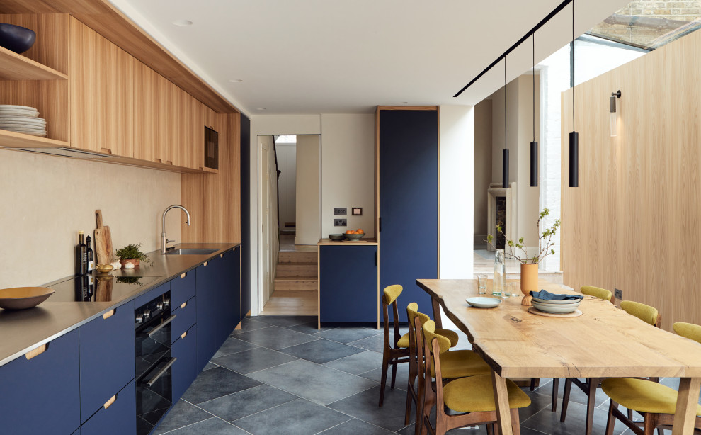 Geschlossene Moderne Küche ohne Insel in U-Form mit Unterbauwaschbecken, flächenbündigen Schrankfronten, blauen Schränken, Edelstahl-Arbeitsplatte, Küchenrückwand in Beige, grauem Boden und grauer Arbeitsplatte in London