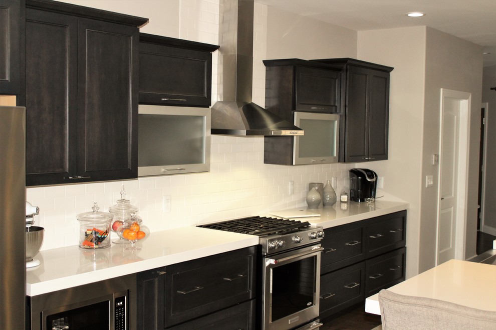 Mid-sized transitional galley medium tone wood floor eat-in kitchen photo in Chicago with a farmhouse sink, recessed-panel cabinets, gray cabinets, quartzite countertops, white backsplash, ceramic backsplash, stainless steel appliances and an island