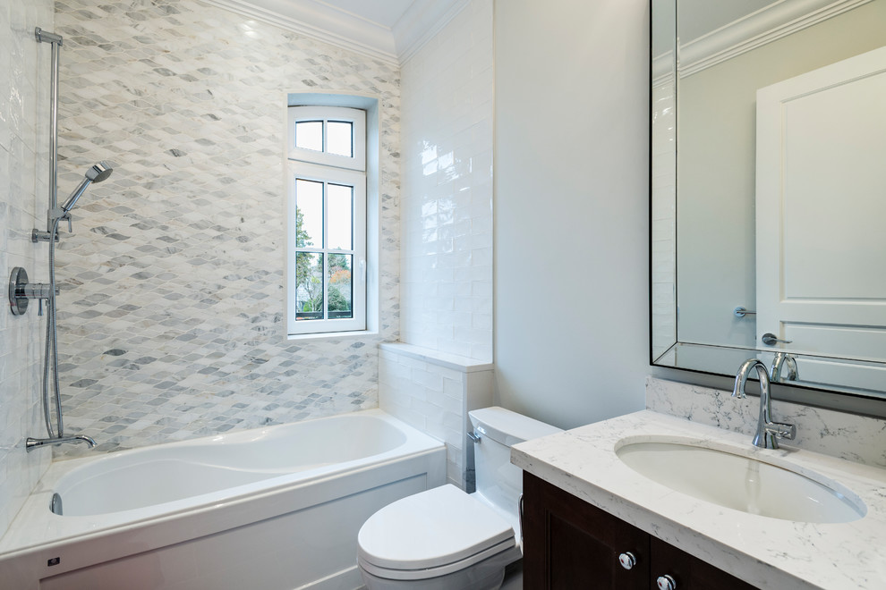 This is an example of a mid-sized traditional 3/4 bathroom in Vancouver with recessed-panel cabinets, black cabinets, an alcove tub, a shower/bathtub combo, a one-piece toilet, gray tile, porcelain tile, white walls, porcelain floors, an undermount sink, engineered quartz benchtops, grey floor and a shower curtain.