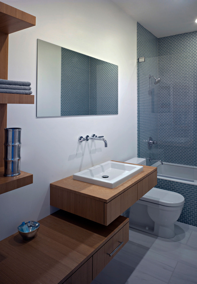 This is an example of a mid-sized modern kids bathroom in Chicago with a drop-in sink, flat-panel cabinets, light wood cabinets, wood benchtops, a drop-in tub, a shower/bathtub combo, a one-piece toilet, gray tile, glass tile, beige walls, porcelain floors, white floor and brown benchtops.