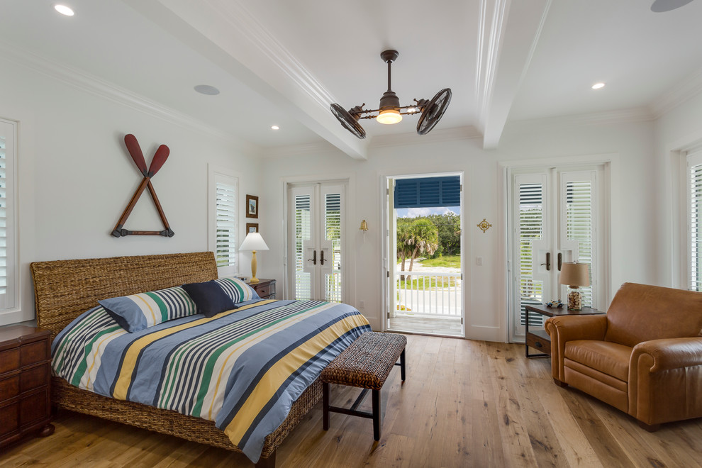 This is an example of a beach style master bedroom in Miami with white walls and light hardwood floors.