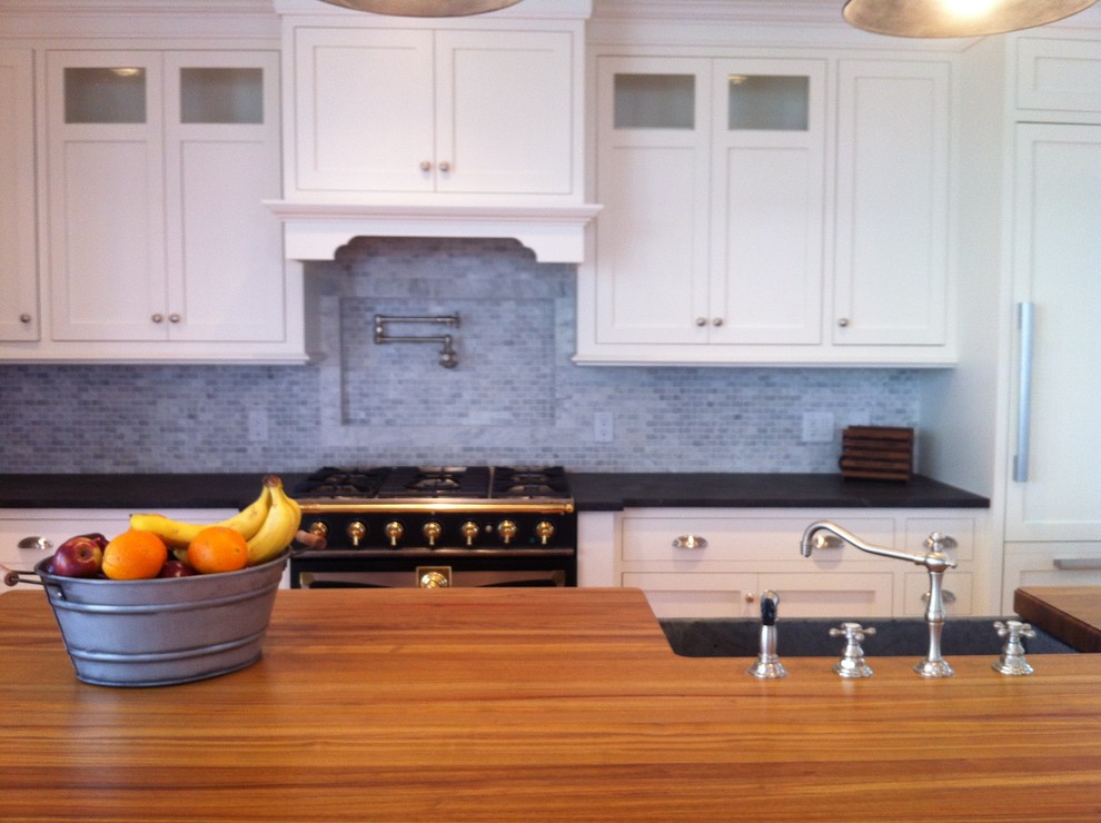 This is an example of an expansive beach style l-shaped open plan kitchen in Boston with a farmhouse sink, shaker cabinets, white cabinets, wood benchtops, grey splashback, medium hardwood floors and with island.