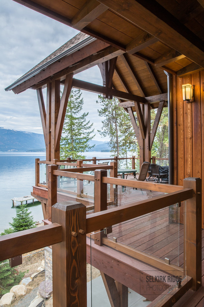 Large elegant two-story and backyard wood brown deck photo with a shingle roof and a roof extension