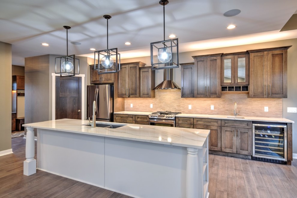 This is an example of an arts and crafts single-wall open plan kitchen in Other with a double-bowl sink, shaker cabinets, dark wood cabinets, quartzite benchtops, beige splashback, stainless steel appliances, medium hardwood floors, with island, brown floor and white benchtop.