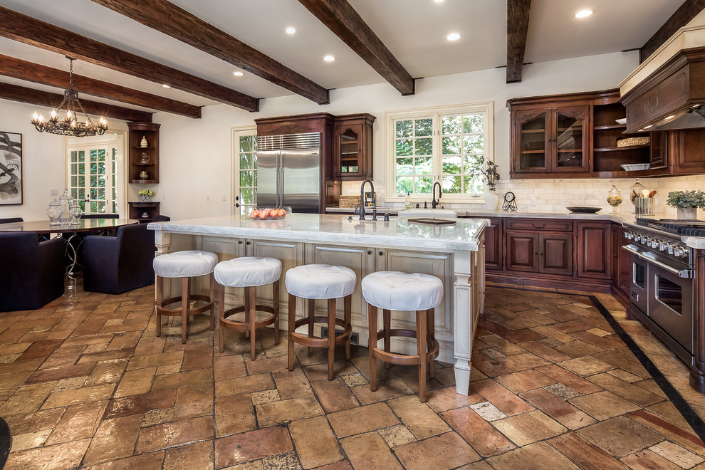 Inspiration for a large mediterranean eat-in kitchen in Los Angeles with dark wood cabinets, marble benchtops, white splashback, ceramic splashback, stainless steel appliances, with island, brown floor and a farmhouse sink.