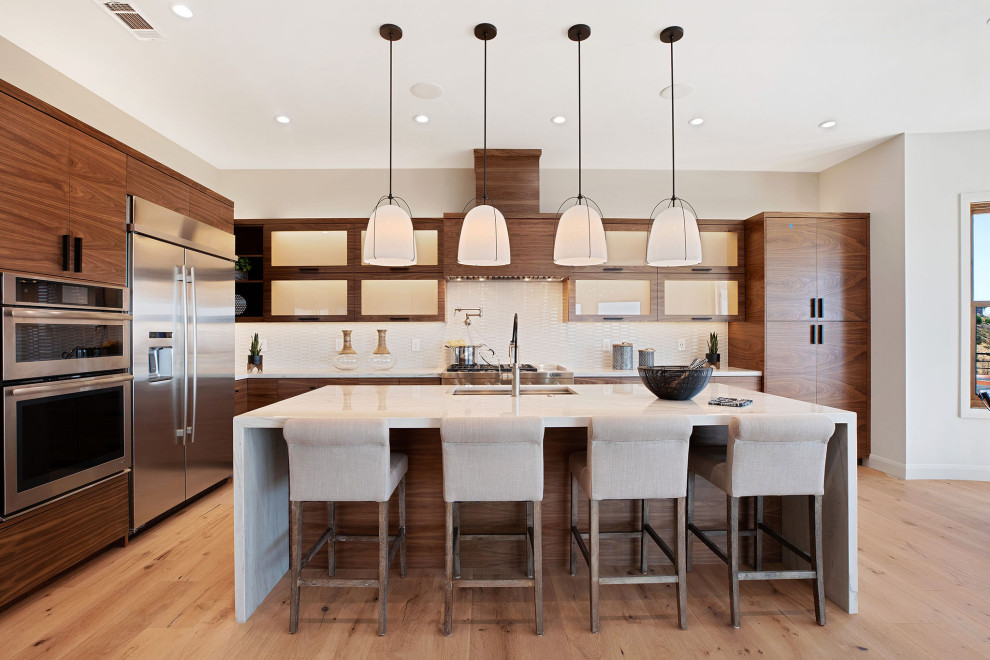 Contemporary l-shaped kitchen in San Francisco with an undermount sink, flat-panel cabinets, medium wood cabinets, white splashback, stainless steel appliances, light hardwood floors, with island, beige floor and white benchtop.
