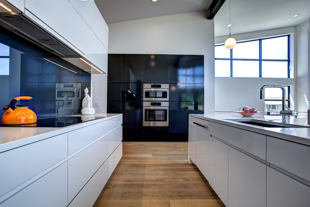 Inspiration for a mid-sized contemporary galley eat-in kitchen in Grand Rapids with an undermount sink, flat-panel cabinets, quartz benchtops, glass sheet splashback, with island, black splashback, stainless steel appliances, light hardwood floors and grey benchtop.