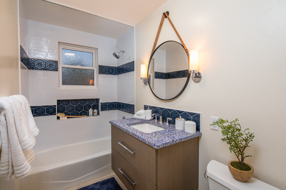Пример оригинального дизайна: маленькая ванная комната в стиле неоклассика (современная классика) с плоскими фасадами, коричневыми фасадами, ванной в нише, душем над ванной, раздельным унитазом, синей плиткой, керамической плиткой, бежевыми стенами, полом из керамогранита, врезной раковиной, столешницей из переработанного стекла, бежевым полом, шторкой для ванной, синей столешницей, нишей, тумбой под одну раковину и подвесной тумбой для на участке и в саду