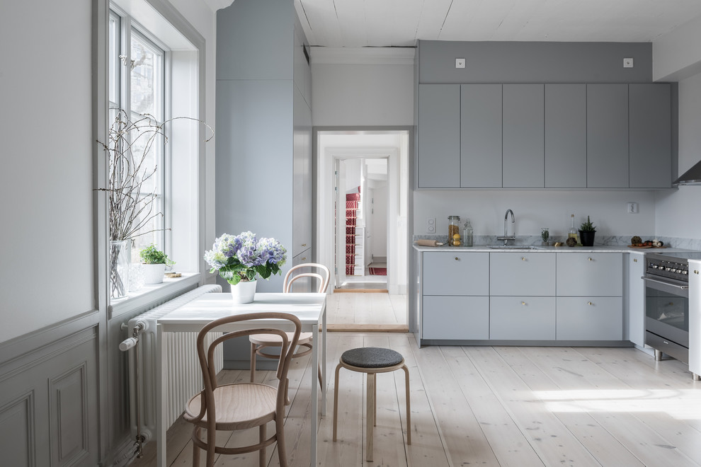 Mid-sized scandinavian l-shaped eat-in kitchen in Stockholm with a single-bowl sink, flat-panel cabinets, blue cabinets, marble benchtops, white splashback, stainless steel appliances, light hardwood floors and no island.
