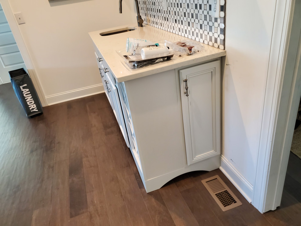 Inspiration for a small craftsman galley laminate floor and brown floor wet bar remodel in Raleigh with an undermount sink, flat-panel cabinets, white cabinets, quartzite countertops, white backsplash, mosaic tile backsplash and white countertops