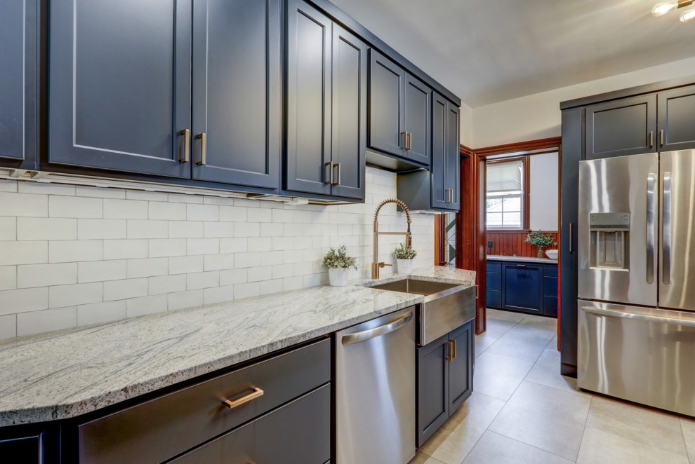 Example of a mid-sized transitional l-shaped vinyl floor and gray floor kitchen pantry design with a farmhouse sink, recessed-panel cabinets, blue cabinets, granite countertops, white backsplash, subway tile backsplash, stainless steel appliances, no island and gray countertops