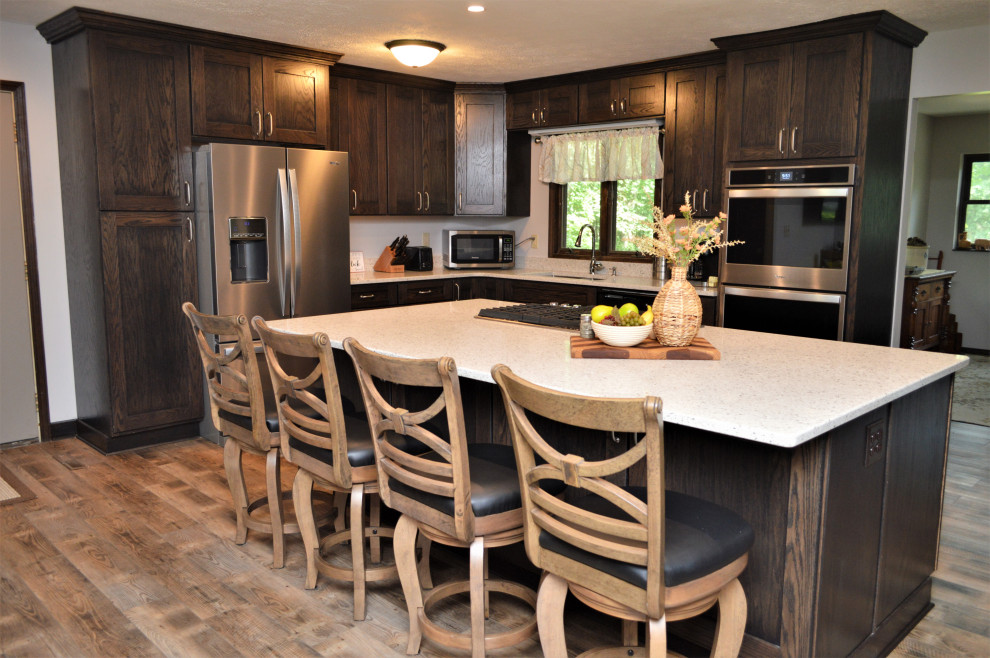Inspiration for a mid-sized country l-shaped open plan kitchen in Chicago with an undermount sink, shaker cabinets, dark wood cabinets, quartzite benchtops, stainless steel appliances, laminate floors, with island, brown floor and grey benchtop.