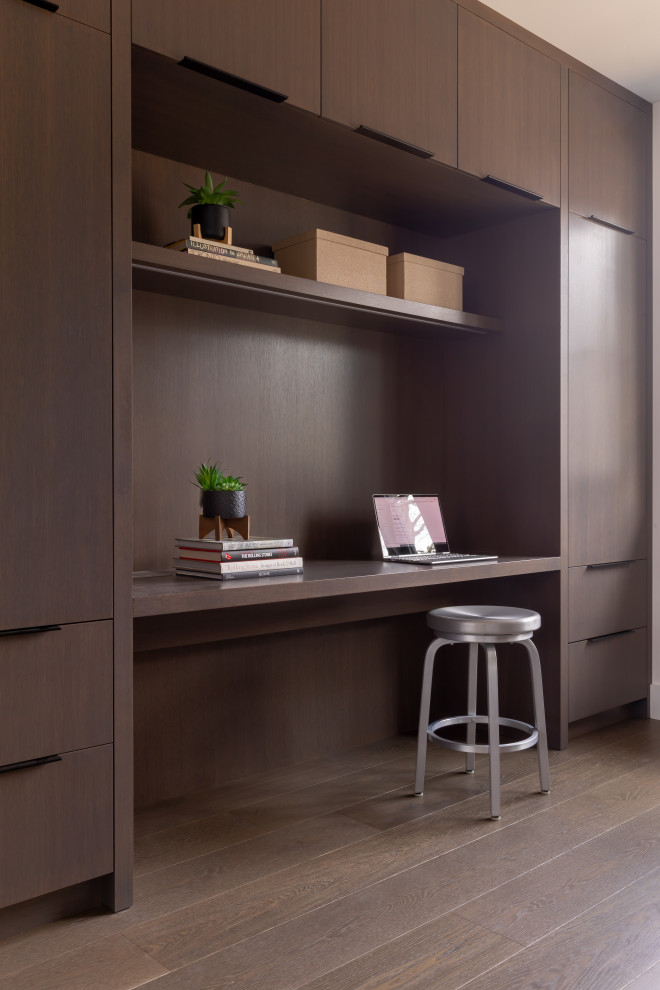 Modelo de despacho contemporáneo con paredes marrones, suelo de madera en tonos medios, escritorio empotrado y suelo marrón