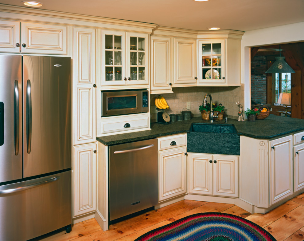 Example of a mid-sized transitional galley light wood floor eat-in kitchen design with a farmhouse sink, raised-panel cabinets, beige cabinets, soapstone countertops, beige backsplash, stone tile backsplash and stainless steel appliances