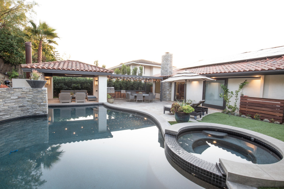 Photo of a modern backyard custom-shaped pool in Orange County with a hot tub and natural stone pavers.