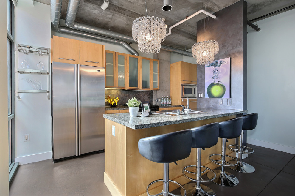 Inspiration for a mid-sized industrial galley kitchen in Denver with a double-bowl sink, flat-panel cabinets, light wood cabinets, marble benchtops, grey splashback, stainless steel appliances, concrete floors and with island.