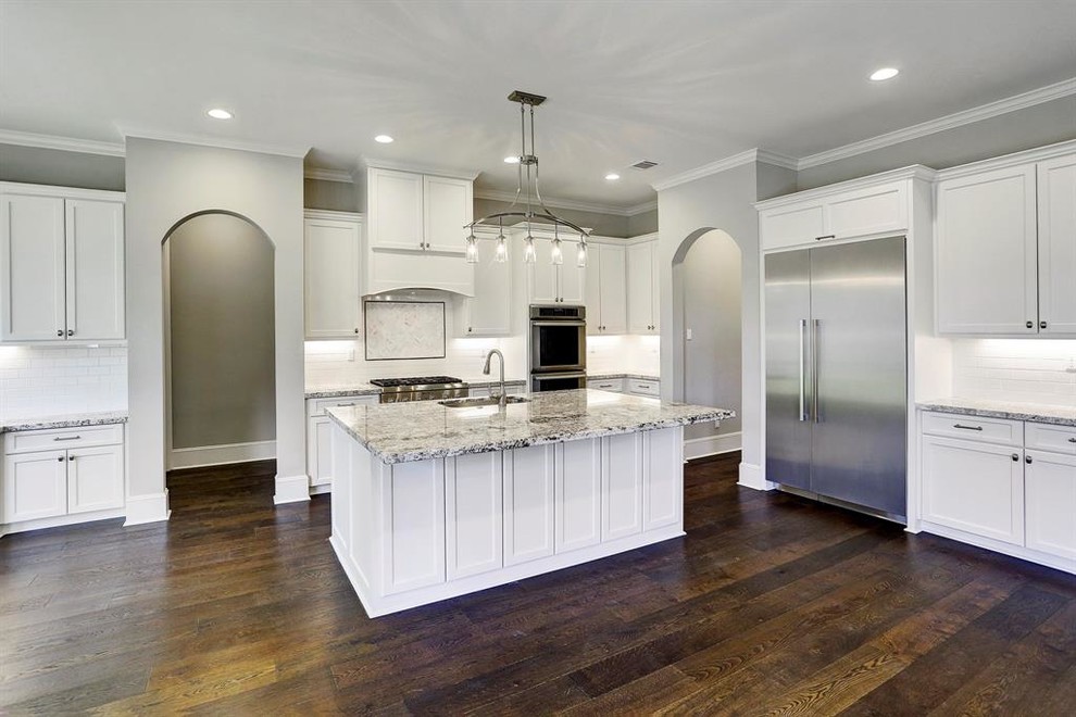 Design ideas for a large contemporary l-shaped open plan kitchen in Houston with an undermount sink, shaker cabinets, white cabinets, granite benchtops, white splashback, subway tile splashback, stainless steel appliances, dark hardwood floors, with island, brown floor and grey benchtop.