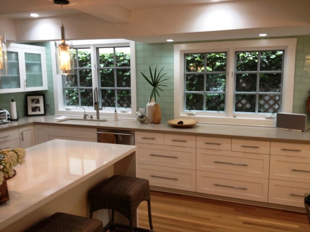 This is an example of a large contemporary l-shaped eat-in kitchen in Orange County with an undermount sink, recessed-panel cabinets, white cabinets, green splashback, stainless steel appliances, with island, glass tile splashback and light hardwood floors.