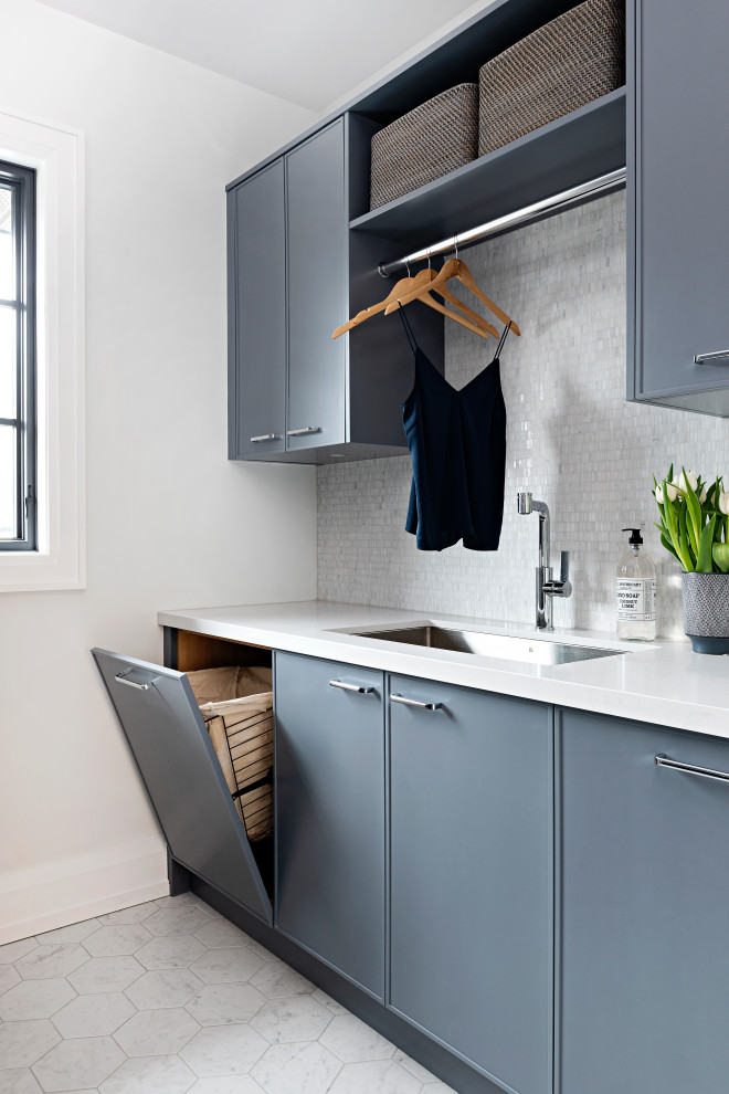 Design ideas for a mid-sized transitional galley laundry room in Toronto with recessed-panel cabinets, blue cabinets, quartz benchtops, white splashback, mosaic tile splashback, ceramic floors, white floor and white benchtop.