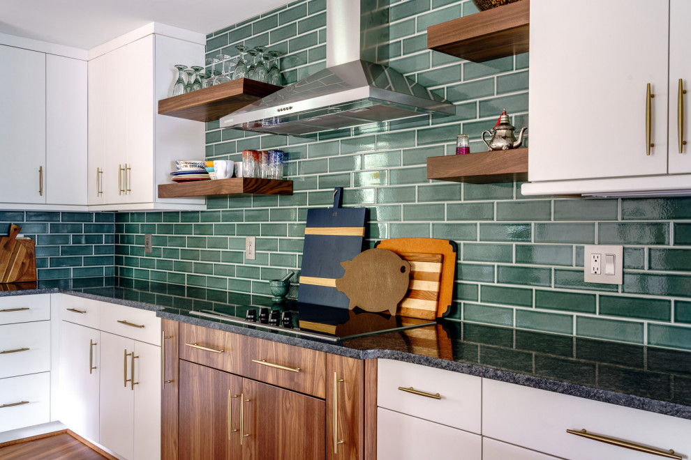 This is an example of a mid-sized midcentury galley eat-in kitchen in Other with a farmhouse sink, flat-panel cabinets, white cabinets, granite benchtops, green splashback, subway tile splashback, stainless steel appliances, laminate floors, with island, brown floor and black benchtop.