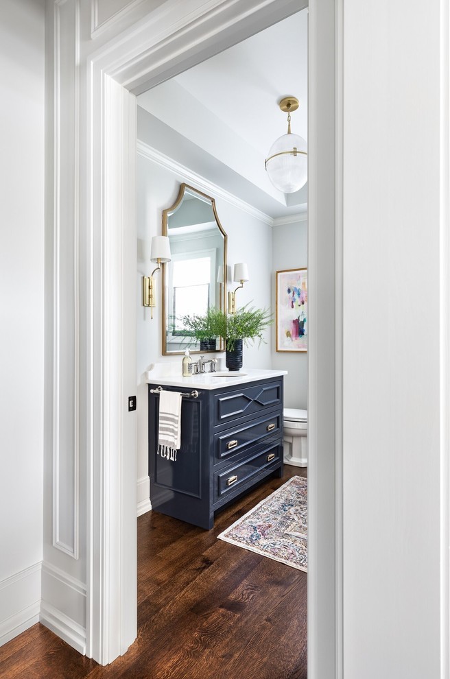 Inspiration for a large transitional powder room in Chicago with furniture-like cabinets, blue cabinets, grey walls, medium hardwood floors, a drop-in sink, engineered quartz benchtops, brown floor and white benchtops.