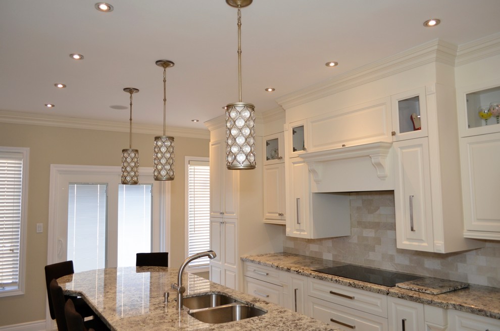 Example of a mid-sized transitional l-shaped porcelain tile enclosed kitchen design in Toronto with an undermount sink, raised-panel cabinets, white cabinets, granite countertops, beige backsplash, stainless steel appliances and an island