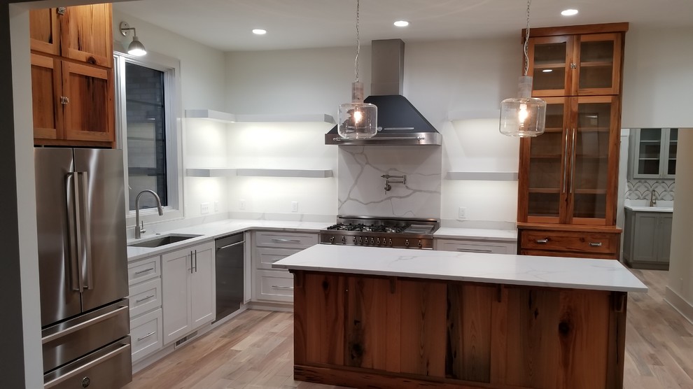 Inspiration for a mid-sized transitional l-shaped light wood floor and brown floor kitchen remodel with an undermount sink, recessed-panel cabinets, white cabinets, marble countertops, white backsplash, marble backsplash, stainless steel appliances, an island and white countertops