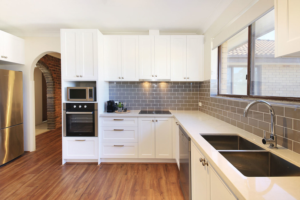 Design ideas for a mid-sized country u-shaped separate kitchen in Sydney with an undermount sink, shaker cabinets, white cabinets, quartz benchtops, ceramic splashback, stainless steel appliances, laminate floors and no island.