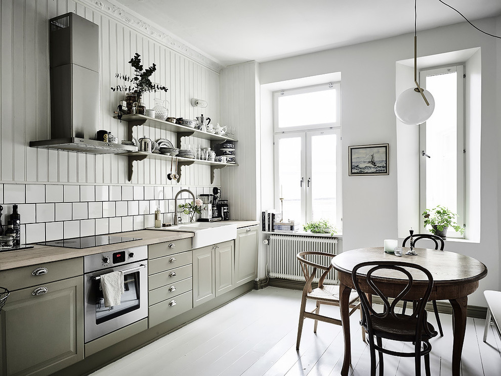 Photo of a mid-sized scandinavian single-wall eat-in kitchen in Gothenburg with a farmhouse sink, wood benchtops, white splashback, ceramic splashback, stainless steel appliances, painted wood floors, no island, raised-panel cabinets and green cabinets.