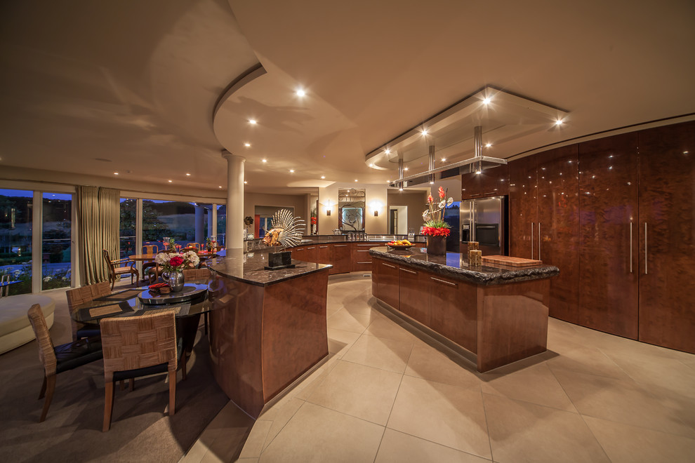 This is an example of a large tropical eat-in kitchen in Auckland with an undermount sink, flat-panel cabinets, medium wood cabinets, granite benchtops, stainless steel appliances, ceramic floors and multiple islands.