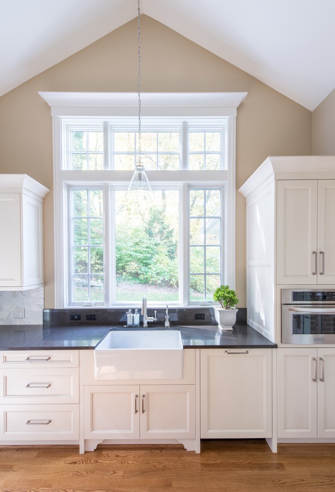 Large transitional u-shaped medium tone wood floor enclosed kitchen photo in DC Metro with a farmhouse sink, shaker cabinets, white cabinets, quartzite countertops, white backsplash, mosaic tile backsplash, stainless steel appliances and an island