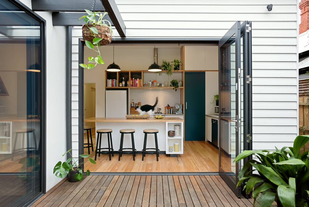 This is an example of a contemporary l-shaped kitchen in Melbourne with flat-panel cabinets, white cabinets, wood benchtops, white splashback, mosaic tile splashback, white appliances, medium hardwood floors, with island, brown floor and brown benchtop.