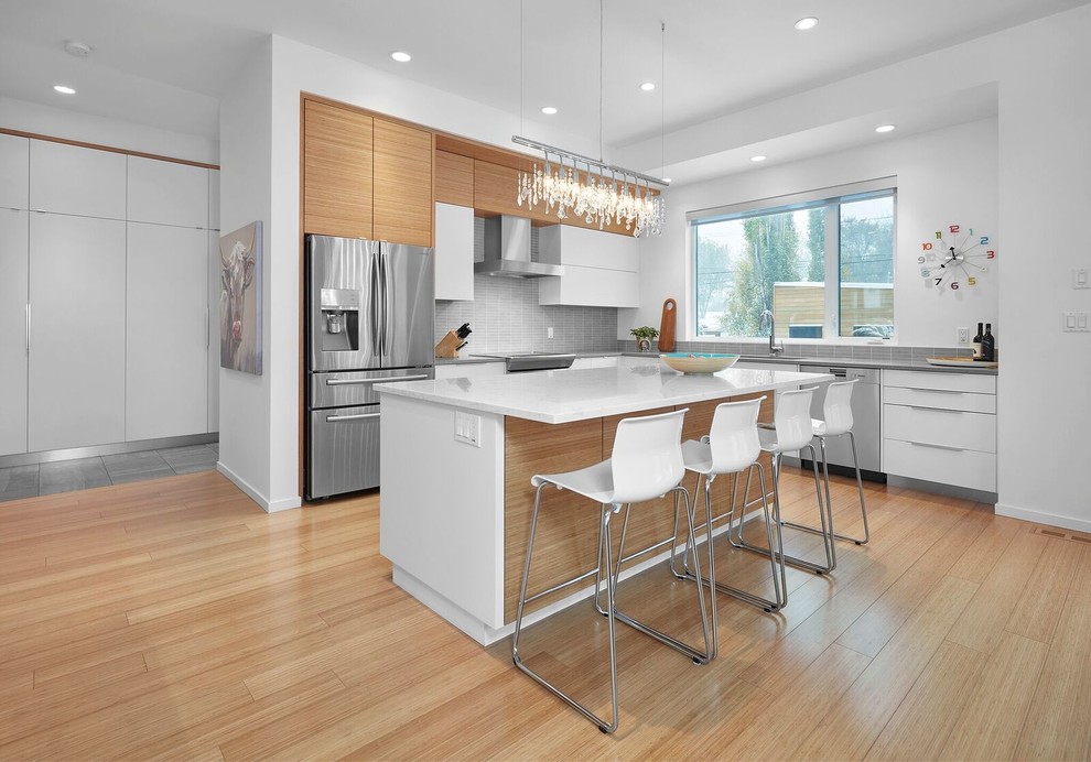 This is an example of a large modern u-shaped open plan kitchen in Calgary with an undermount sink, flat-panel cabinets, white cabinets, quartz benchtops, grey splashback, matchstick tile splashback, stainless steel appliances, light hardwood floors, with island and brown floor.