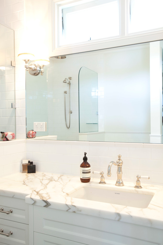 Mid-sized contemporary master bathroom in Brisbane with recessed-panel cabinets, white cabinets, a freestanding tub, a double shower, a two-piece toilet, white tile, ceramic tile, white walls, ceramic floors, an undermount sink and marble benchtops.