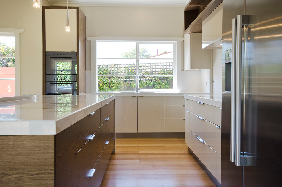 Photo of a mid-sized contemporary l-shaped eat-in kitchen in Melbourne with an undermount sink, flat-panel cabinets, marble benchtops, beige splashback, stone slab splashback, stainless steel appliances, medium wood cabinets, medium hardwood floors and with island.