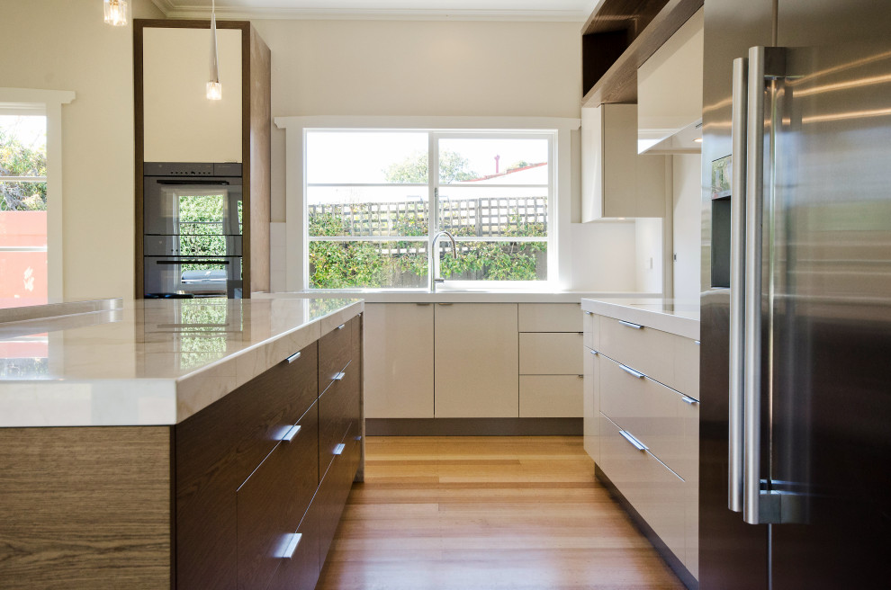 Photo of a large contemporary l-shaped eat-in kitchen in Melbourne with an undermount sink, flat-panel cabinets, marble benchtops, stone slab splashback, stainless steel appliances, medium wood cabinets, medium hardwood floors, with island, white splashback and white benchtop.