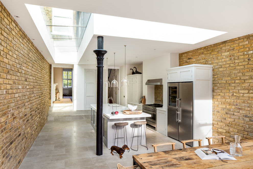 Mid-sized transitional eat-in kitchen in London with an integrated sink, shaker cabinets, grey cabinets, solid surface benchtops, stainless steel appliances, limestone floors and with island.