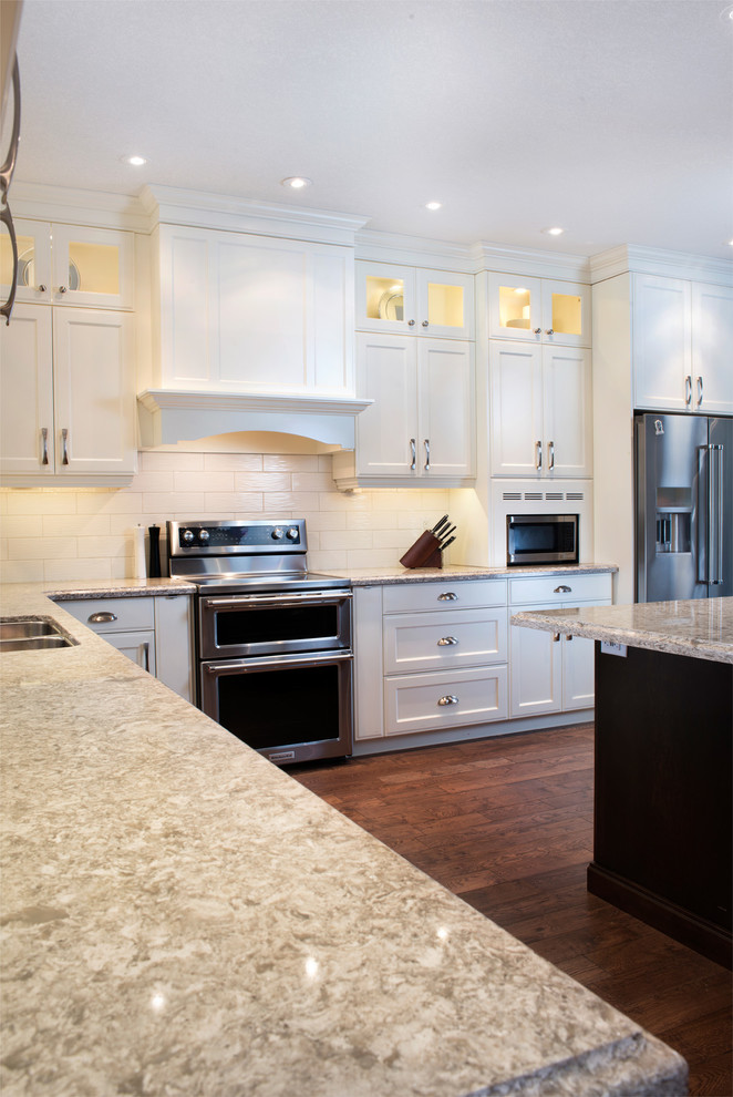 Inspiration for a large transitional l-shaped medium tone wood floor kitchen remodel in Toronto with an undermount sink, recessed-panel cabinets, white cabinets, quartz countertops, white backsplash, subway tile backsplash, stainless steel appliances and an island