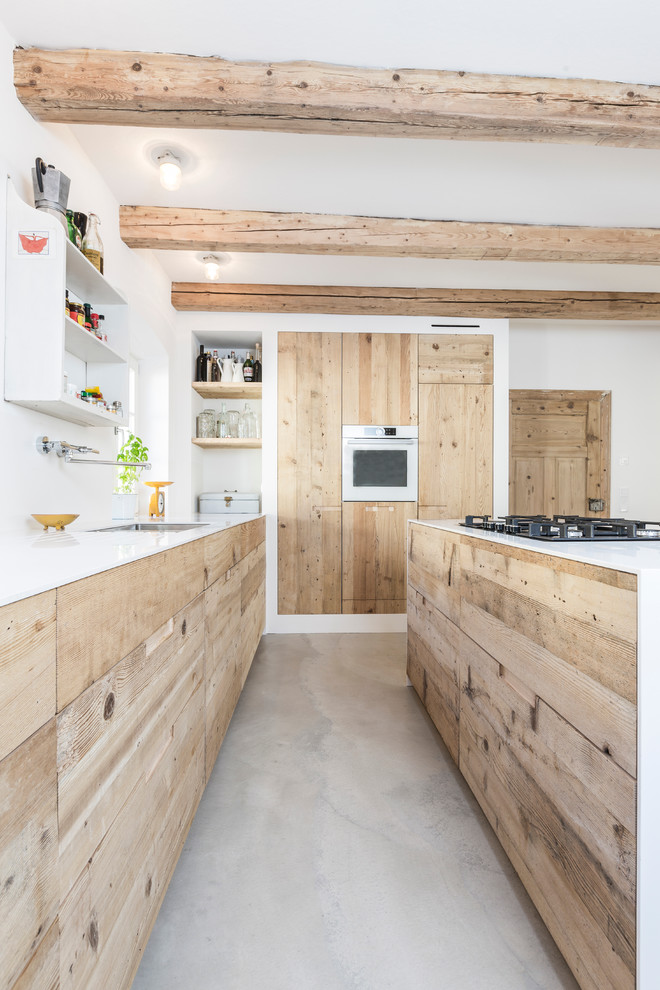 Inspiration for a large industrial galley open plan kitchen in Munich with an undermount sink, flat-panel cabinets, light wood cabinets, solid surface benchtops, concrete floors and with island.