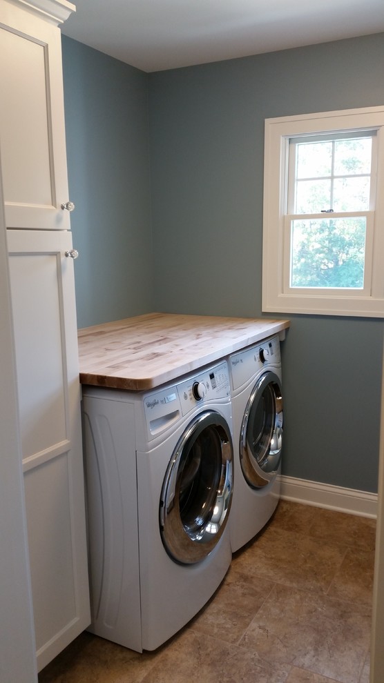 Design ideas for a small transitional single-wall laundry cupboard in Chicago with a farmhouse sink, recessed-panel cabinets, white cabinets, wood benchtops, grey walls, ceramic floors, a side-by-side washer and dryer, brown floor and beige benchtop.
