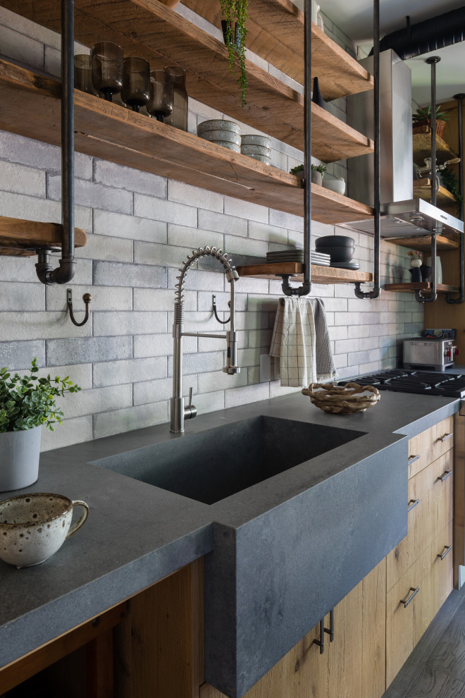 This is an example of a mid-sized industrial single-wall eat-in kitchen in Other with a drop-in sink, light wood cabinets, grey splashback, brick splashback, stainless steel appliances, medium hardwood floors, with island, brown floor, grey benchtop, beaded inset cabinets and concrete benchtops.
