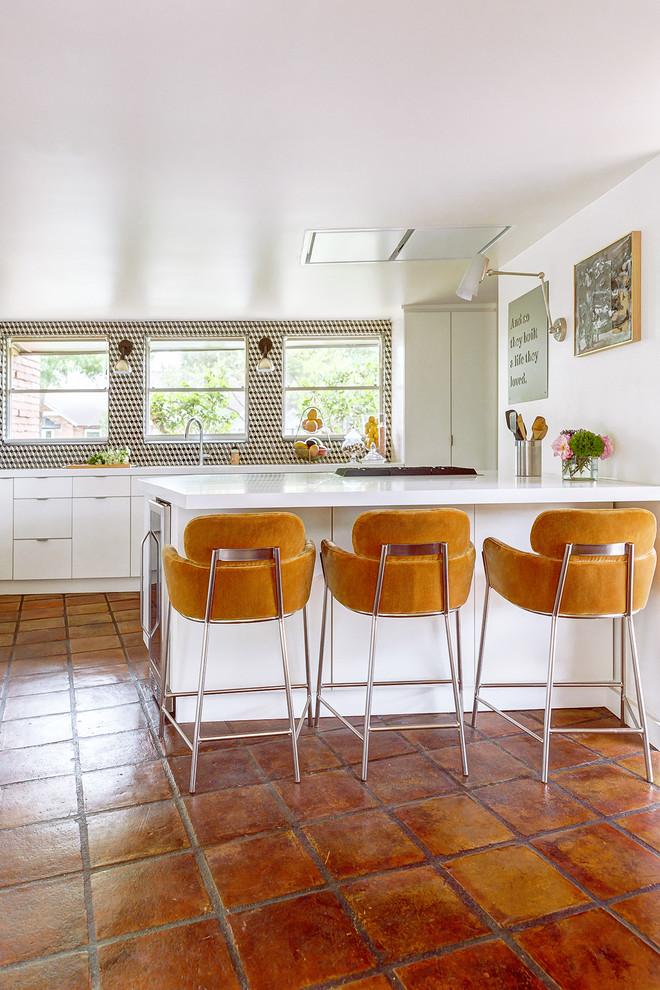 Inspiration for a large midcentury galley kitchen in Houston with a double-bowl sink, flat-panel cabinets, white cabinets, solid surface benchtops, multi-coloured splashback, mosaic tile splashback, stainless steel appliances, terra-cotta floors, with island, brown floor and white benchtop.
